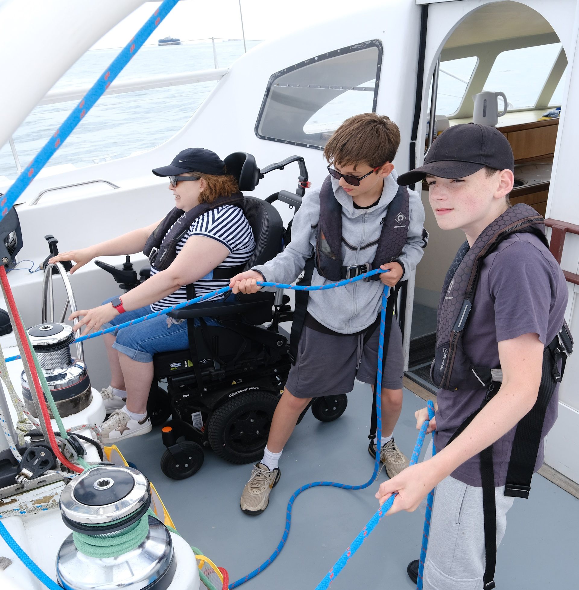 Young sailors, including a powered-wheelchair user, working the ropes on the accessible deck